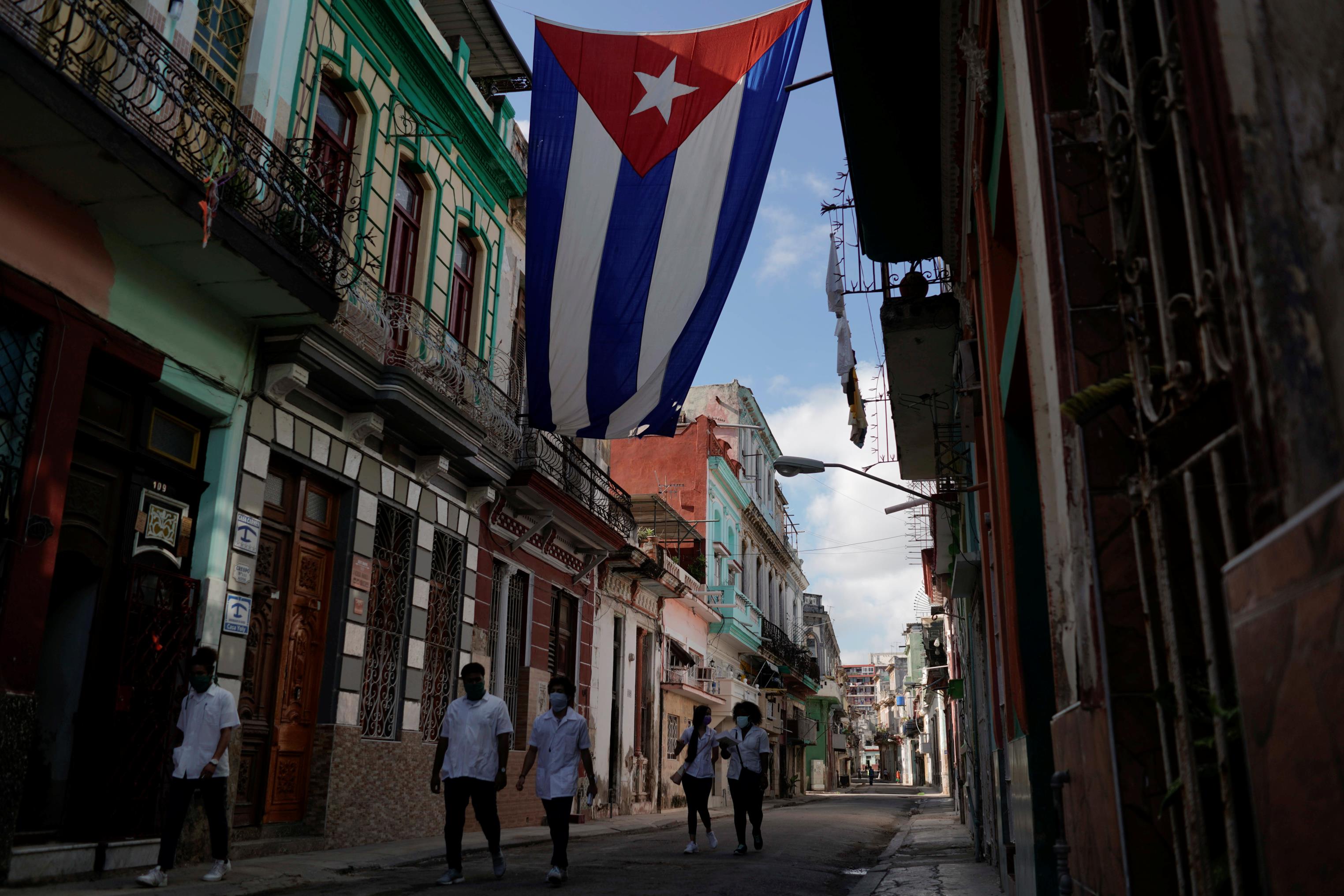 Medical students walk past a Cuban flag as they check door-to-door for people with symptoms amid co<em></em>ncerns a<em></em>bout the spread of the coro<em></em>navirus disease (COVID-19), in downtown Havana, Cuba, May 12, 2020. REUTERS/Alexandre Meneghini