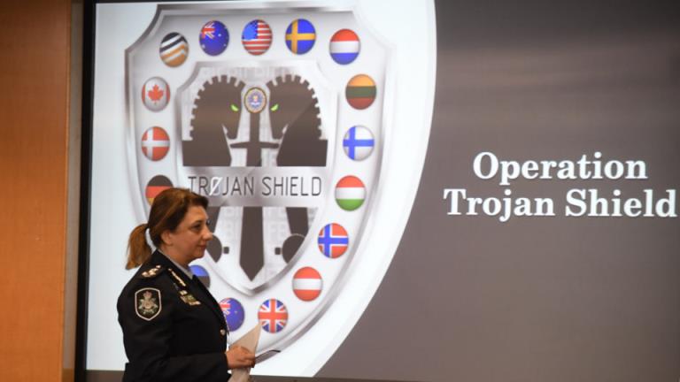 Commander Xenia Cotter, from the Australian Federal Police, walks past an Operation Trojan shield logo during a news conference, Tuesday, June 8, 2021, in San Diego. The global sting operation involved an encrypted communications platform developed by the FBI and sparked a series of raids and arrests around the world in which more than 800 suspects were arrested and more than 32 tons of drugs — cocaine, cannabis, amphetamines and methamphetamines were seized.