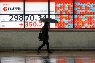 A man holding an umbrella walks in front of an electric board showing Nikkei index at a brokerage in Tokyo, Japan February 15, 2021. REUTERS/Kim Kyung-Hoon