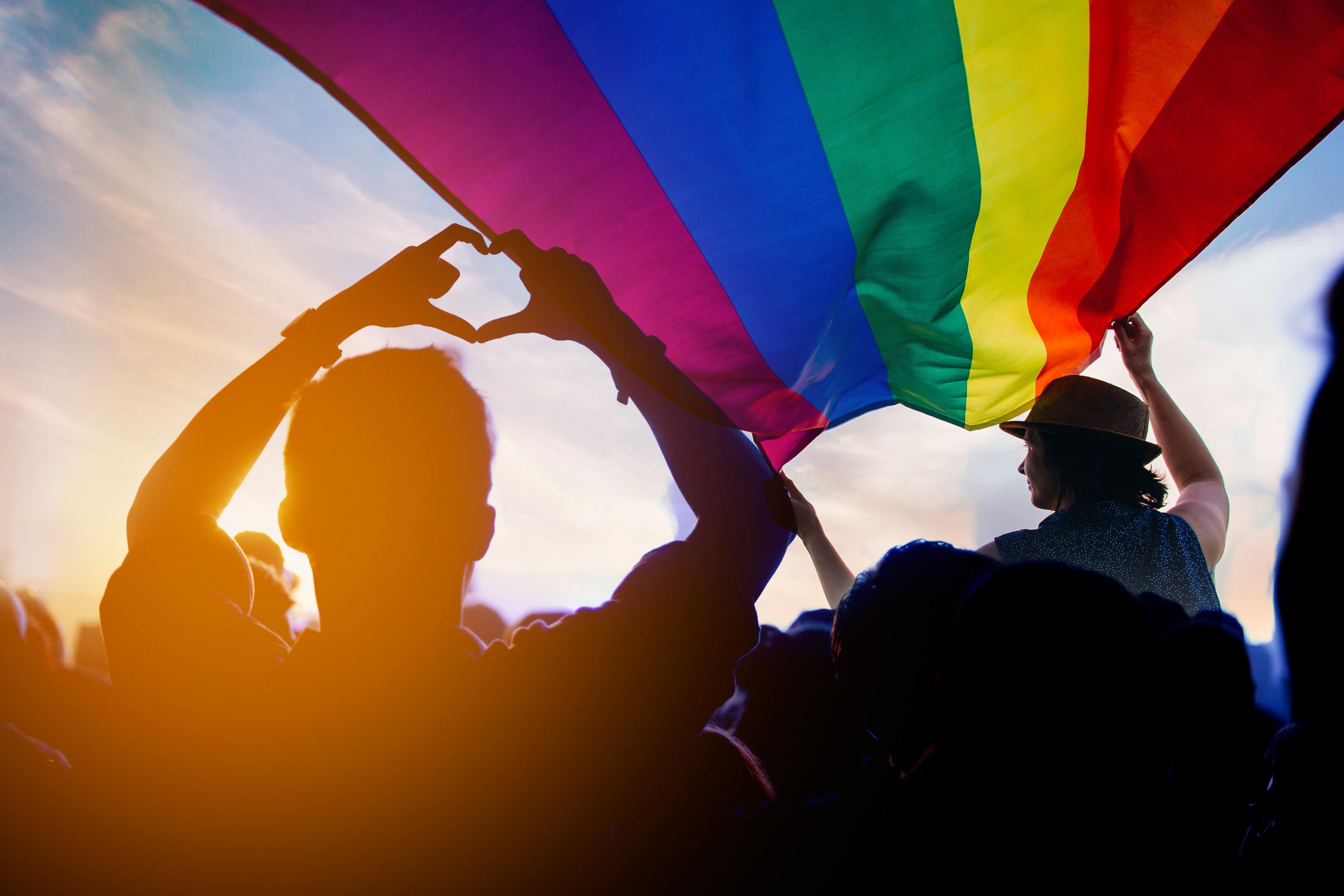 silhouetted people beneath gay pride flag